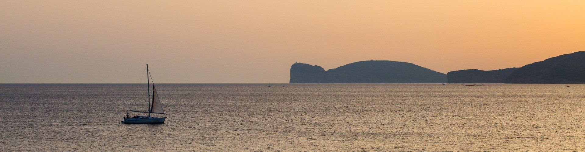 Das Meer bei Alghero beim Sonnenuntergang mit einem Segelboot und der Silhouette vom Capo Caccia