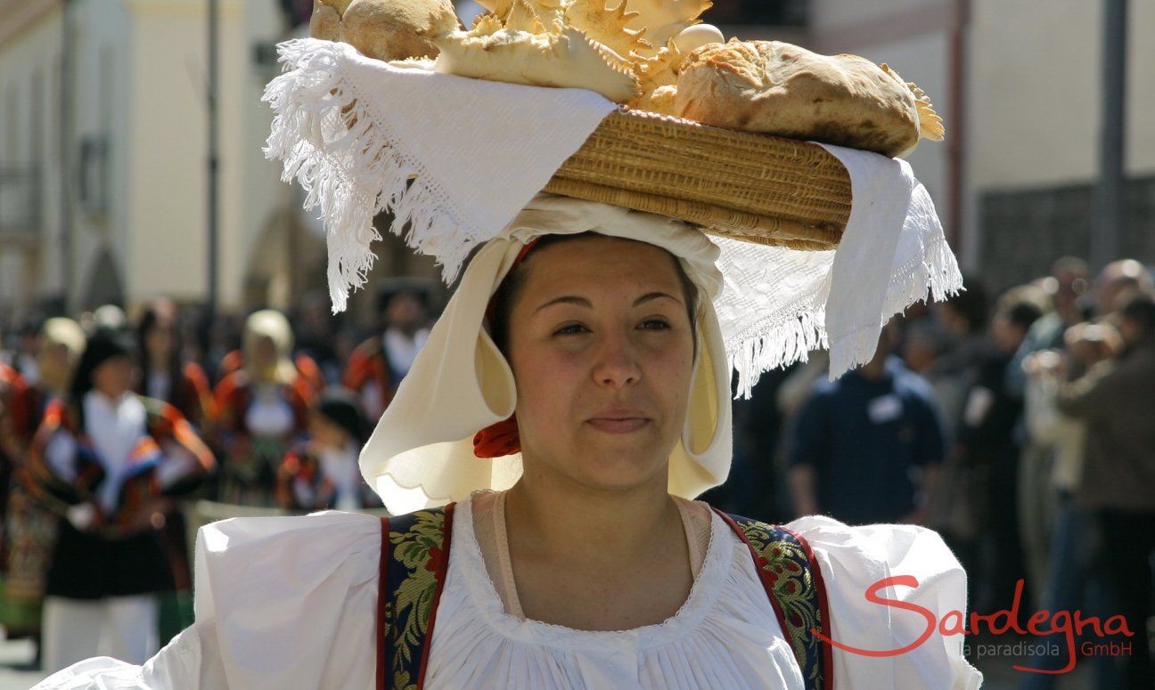 Frau in sardischer Tracht, die auf traditionelle Art einen Korb mit Festtagsbrot auf dem Kopf trägt
