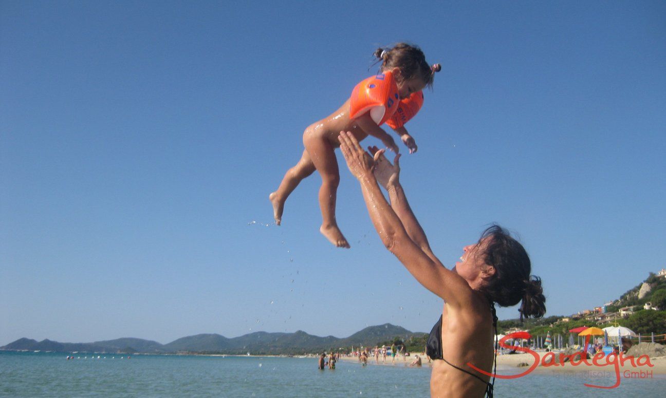 Mutter wirft ihr Baby in die Luft am Meer bei Monte Nai