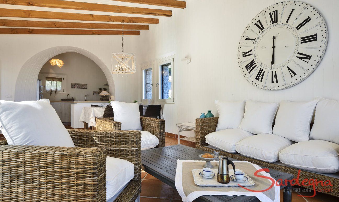 Li Conchi 10 | Sofaecke mit großer Wanduhr und Essbereich im Hintergrund Sofaecke unter einer großen Wanduhr Li Conchi 10, Cala Sinzias