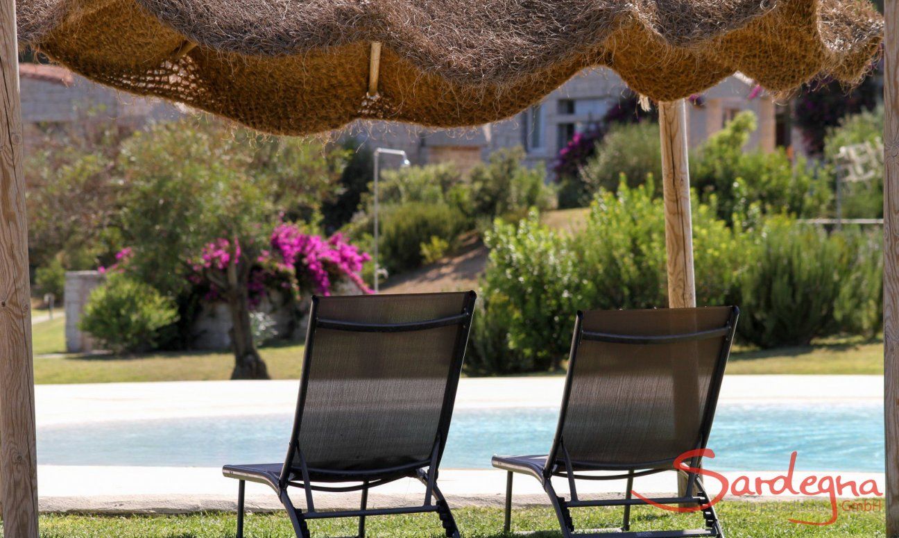 Sonnenliegen unter einem Bastsonnenschirm am Pool von Li Conchi