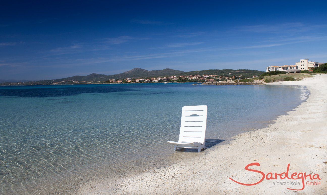 Weißer Sonnenstuhl im seichten, glasklaren Meerwasser am Strand von Golfo Aranci