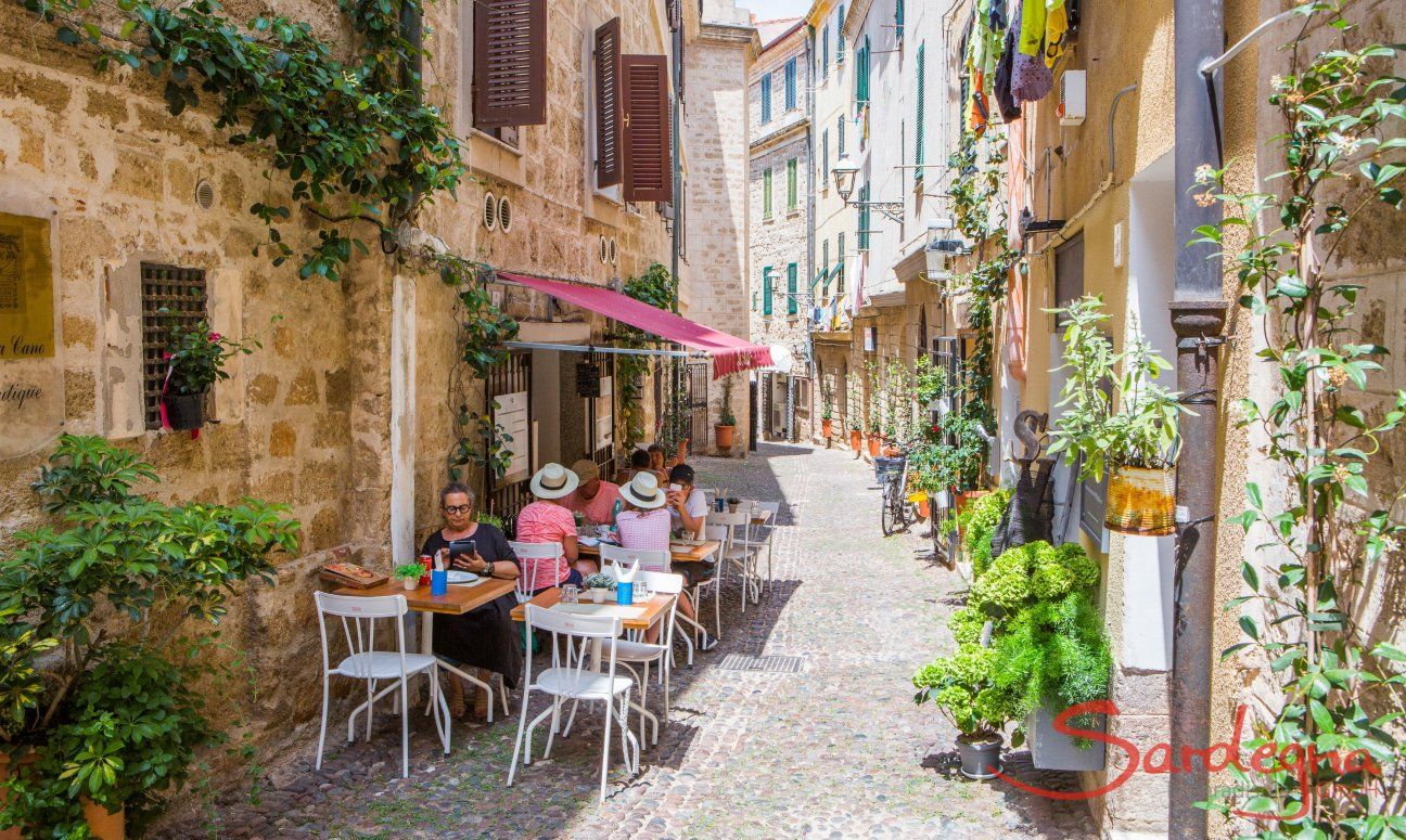 Schmale, autofreie Gass in Alghero mit Tischen eines Restaurants auf der kopfsteingepflasterten Staße