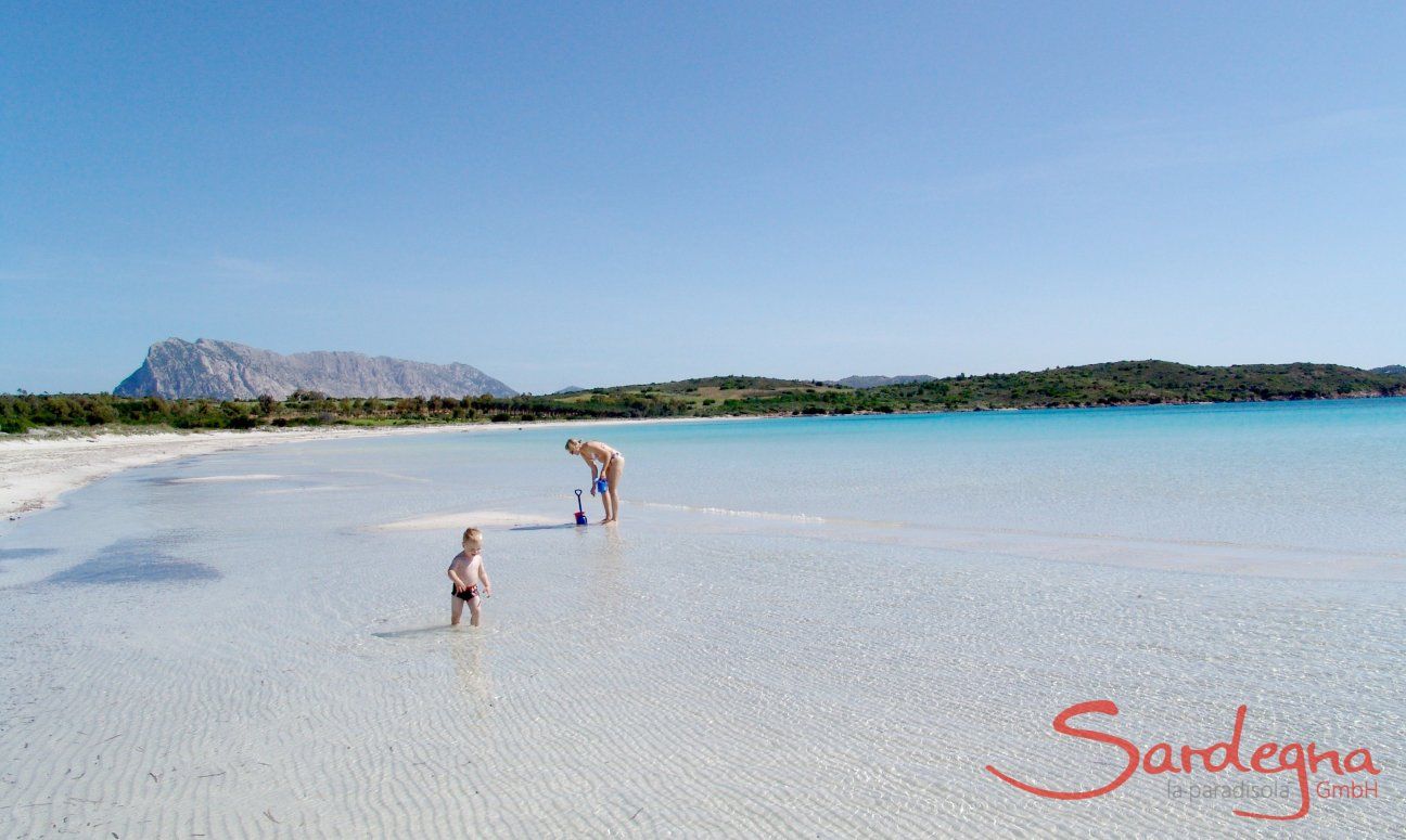 Mutter mit kleinem Kind im glasklaren, seicht abfallenden Wasser von Cala Brandinchi