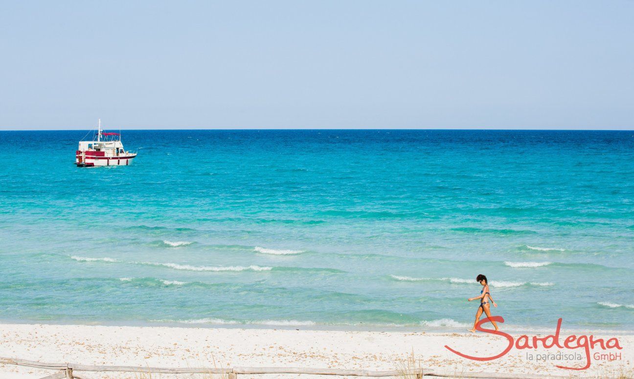 Frau läuft am weißen Strand von La Cinta vor dem hellblauen Meer mit einem weiß und roten Boot