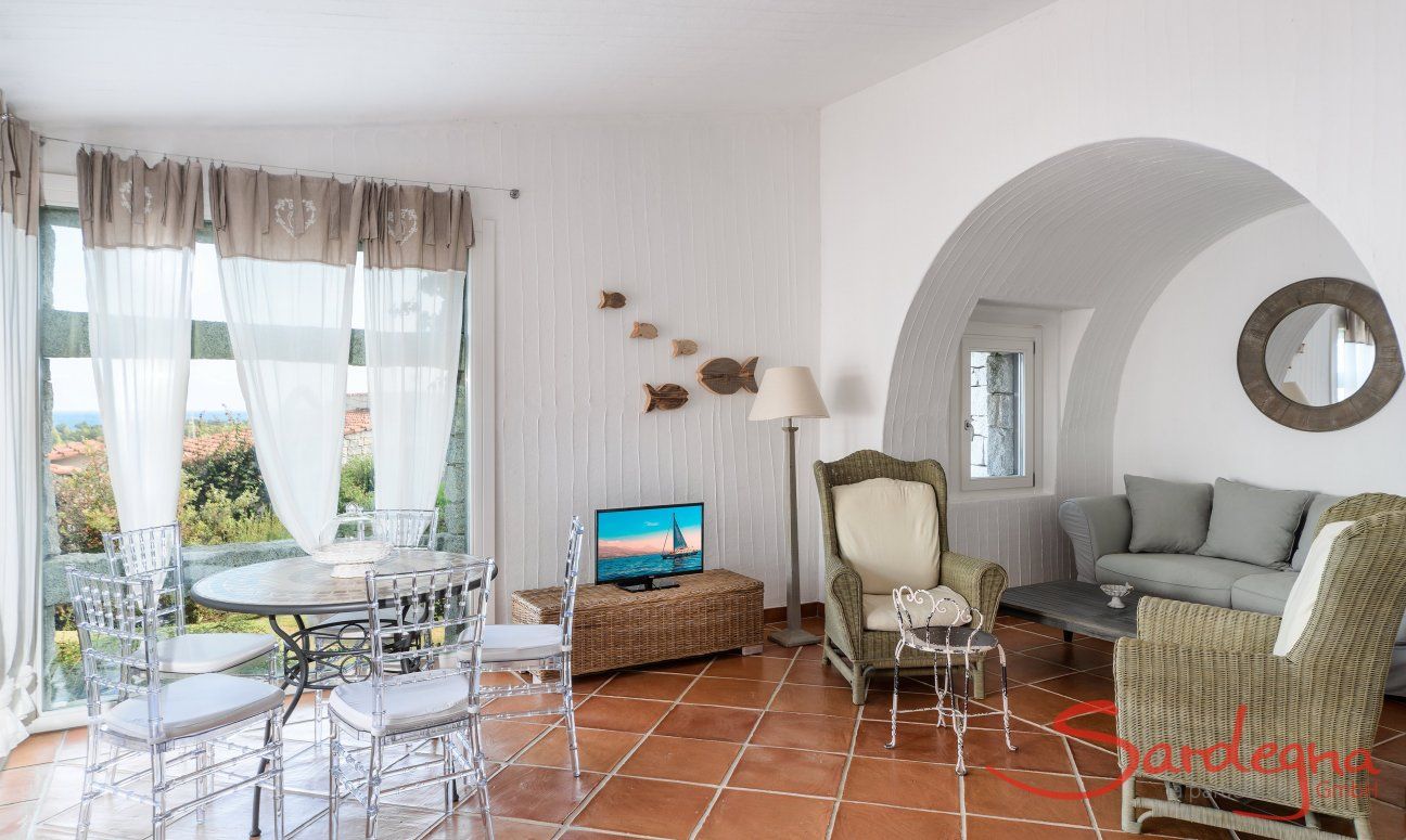Li Conchi 30 | Wohnzimmer mit Panoramafenster, rundem Tisch mit Stühlen, TV und Sofaecke unter einem großen Wandbogen Hausdarstellung von Li Conchi 30