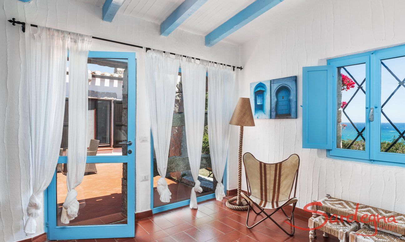 Casa 17 | Wohnzimmer mit Fensterfront zur Terrasse und zum Meer und Lesesessel Casa 17, Sant Elmo, Südsardinien