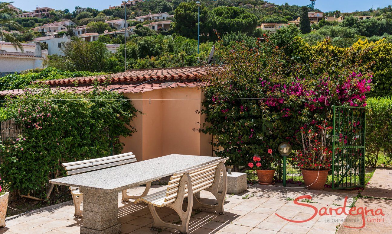 Villa Palme | Großer, stabiler Granittisch inmitten blühenden, mediterranen Planzen mit Blick auf die Hügel von Costa Rei Villa Palme, Costa Rei