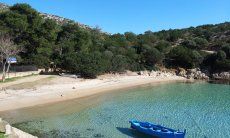 Blaues Fischerboot schwebt im glasklaren Wasser der Bucht Cala Moresca bei Golfo Aranci