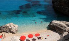 Drei rote, schattenspendende Sonnenschirme am pardiesischen Strand von Cala Goloritze; Cala Luna