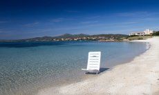 Weißer Sonnenstuhl im seichten, glasklaren Meerwasser am Strand von Golfo Aranci