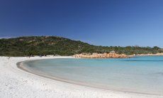 Halbmondförmiger, weißer Sandstrand Romanzzino endet in gelben Felsen und einem Hügel mit grüner Macchia