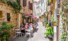 Schmale, autofreie Gass in Alghero mit Tischen eines Restaurants auf der kopfsteingepflasterten Staße