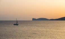 Das Meer bei Alghero beim Sonnenuntergang mit einem Segelboot und der Silhouette vom Capo Caccia