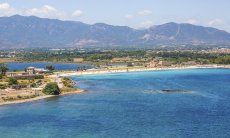 Strand von Nora mit dem Ort Pula und Bergen im Hintergrund