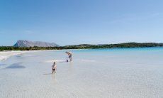 Mutter mit kleinem Kind im glasklaren, seicht abfallenden Wasser von Cala Brandinchi