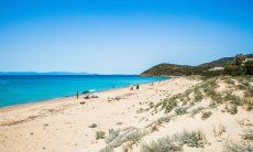 Breiter weißer Sandstrand von Geremeas mit blauem Meer und der Küste von Cagliari im Hintergrund