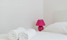 Villa Pola | Weißes Bett mit Handtüchern und Nachttischlampe in pink Weißes Bett mit Handtüchern und Nachttischlampe in pink