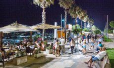Alghero bei Nacht: Besucher flanieren and der von Lanternen erleuchteten Hafenpromenade mit hohen Palmen