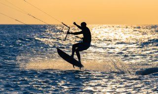 Kitezone Sardegna | Sardinien Chia | Kitesurfer hebt ab vor dem gelben Himmel der Abendsonne